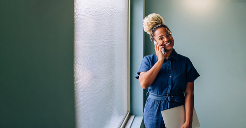 Smiling young professional woman on a phone call holding a laptop