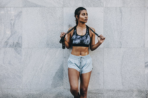 Woman in fitness clothes standing against a wall holding a skipping rope