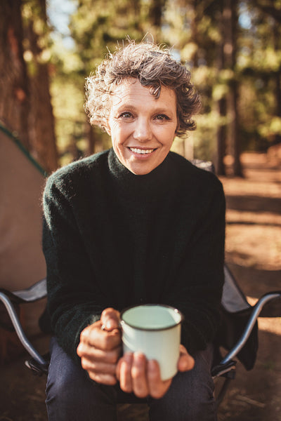 Senior woman sitting outside the tent with a cup of coffee