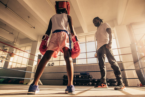 Rear view of a boxing kid standing inside a boxing ring with his trainer