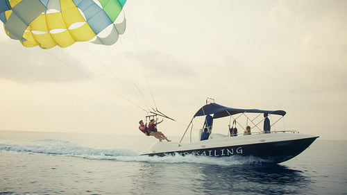 Two people parasailing high above the ocean towed by a boat