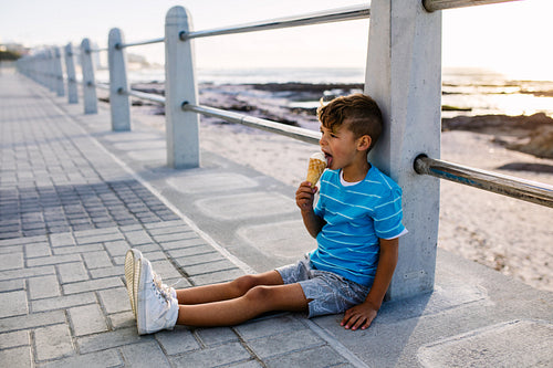 Boy eating an ice cream sitting near seashore