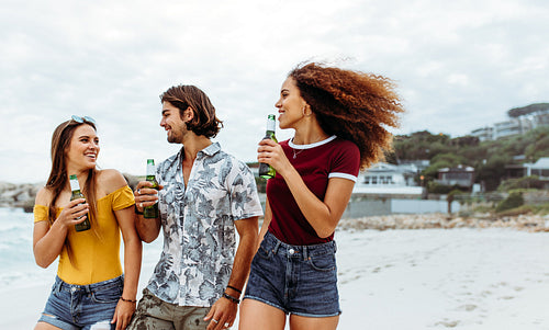 Multi-ethnic friends with beers walking along the beach