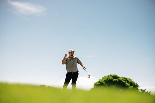 Triumphant sportsman celebrates victory with a fist pump at a sunny golf resort.