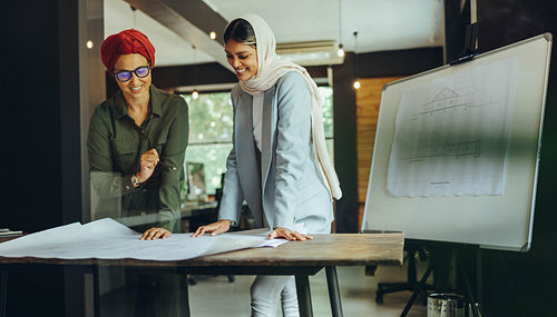 Cheerful female architects working on blueprint drawings in an o