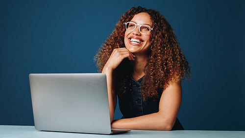 Woman working on laptop in studio with glasses and smiling expression