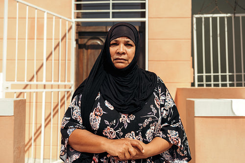 Muslim woman looking at the camera while standing outside her home