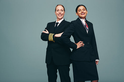 Pilot and air hostess smiling at the camera in a studio