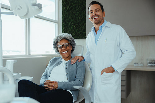 Male dentist standing with his female senior patient in a bright modern dental office