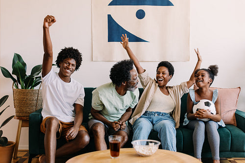 Black family celebrating while watching soccer game on the couch