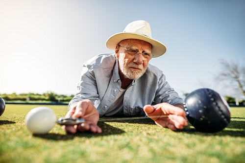 Close up of an old man measuring the distance between the boules