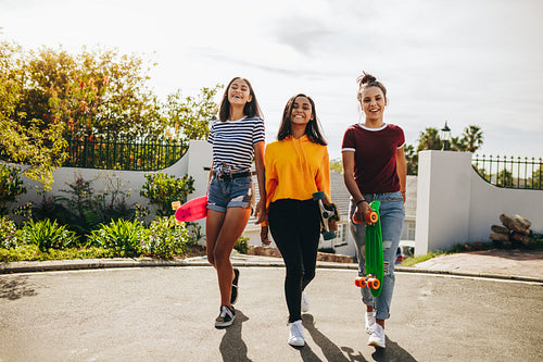 Teenage girls walking holding skateboards