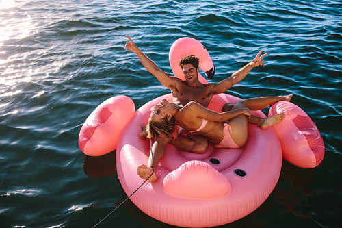 Excited couple riding on inflatable toy behind a boat