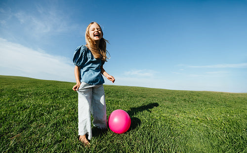 Girl laughing with pink ball in sunny field