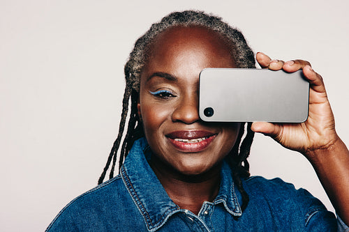Mature woman holding a smartphone over her eye