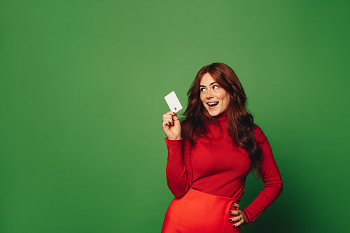 Fashionable woman holding a credit card for shopping on a green studio background
