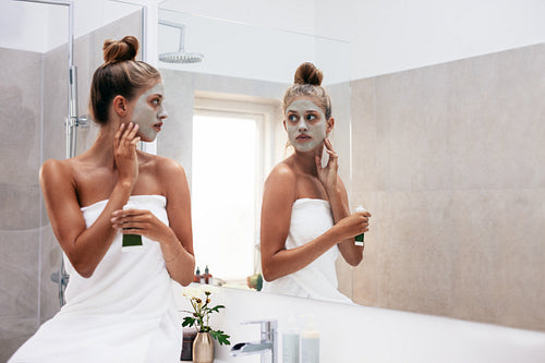 Young woman wrapped in towel applying facepack
