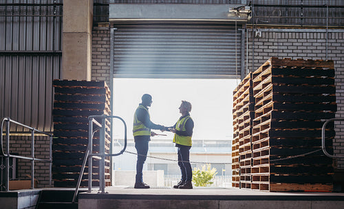 Happy logistics partners shaking hands at a loading dock