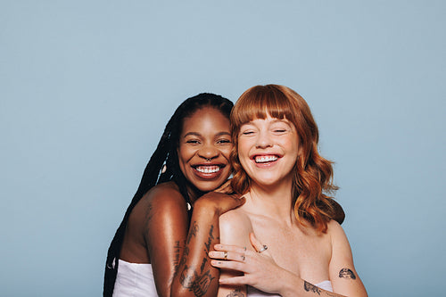 Two women with different skin tones standing together in a studio