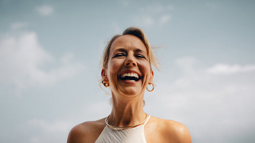 Smiling woman wearing elegant jewelry under a bright blue sky