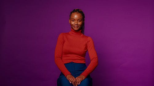 Young woman smiles and laughs on a stool against a purple backdrop