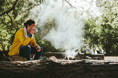 Man camping in forest sitting near a bonfire