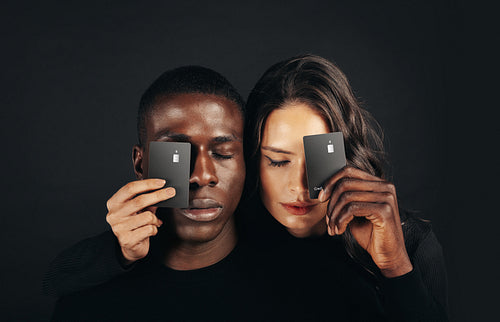 Couple with exclusive credit cards standing in a studio with their eyes closed