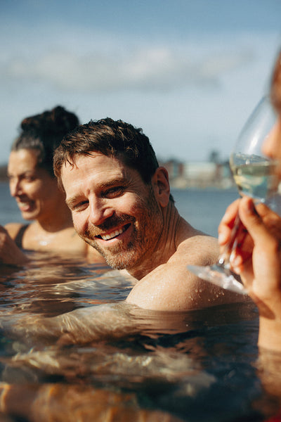 A smiling man shares spa wellness with friends in outdoor water.