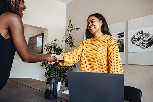 Two professionals shaking hands in creative office setting with architectural designs