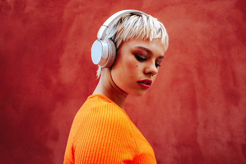 Young woman wears headphones while listening to music against red background