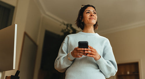 Business woman holds a smartphone and looks upward in the office for a portrait