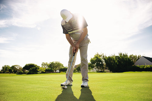 Man on the putting green playing golf amidst beaming rays outdoors during summer