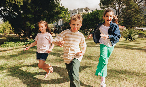 Three children running together outdoors on a sunny day