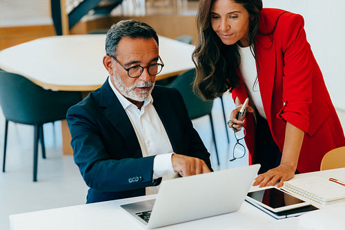 Senior professionals discussing documents while working on a laptop at the office