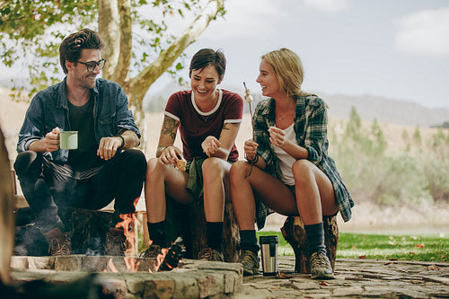 Friends camping in the countryside toasting food on bonfire.