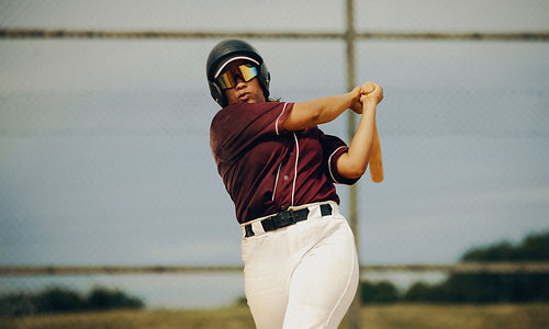 Young baseball player swinging bat and wearing maroon jersey