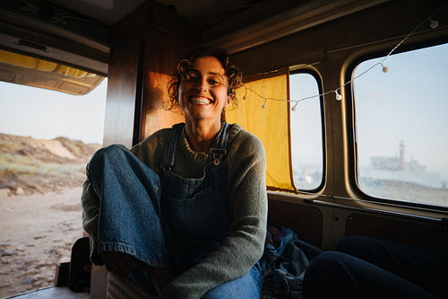 A joyful woman smiles inside a vintage van by the sea