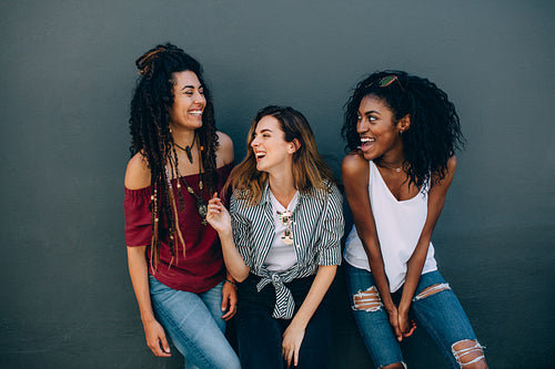 Friends in fashionable clothing standing against a wall