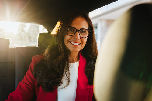 Businesswoman in a red blazer smiling from the backseat of a car