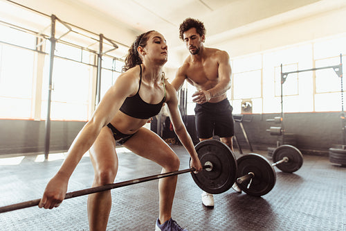 Personal trainer with woman lifting barbell