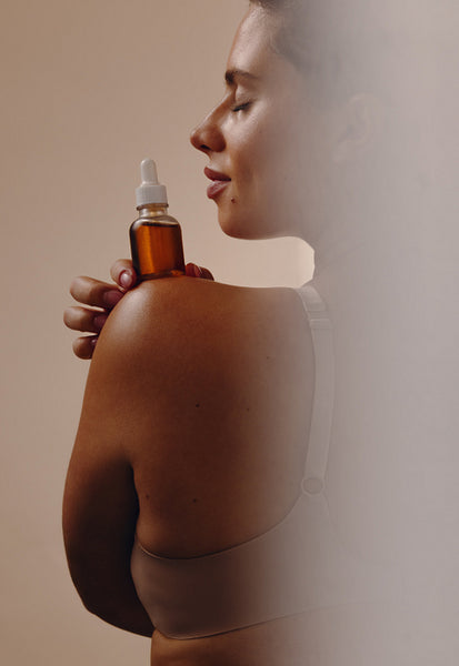 Woman holding skincare serum on shoulder with closed eyes