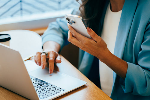 Business professional working on a laptop while checking a mobile device