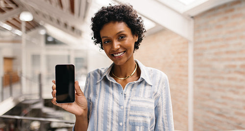Cheerful small business owner showing a smartphone in a warehouse