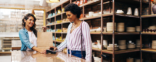 Satisfied female shopper doing an NFC payment in a ceramic store