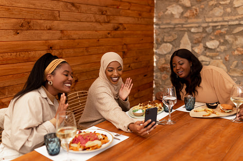 Ethnic female friends having a video call in a restaurant