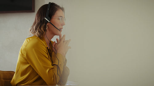 Businesswoman in headset gestures while working on computer in home office