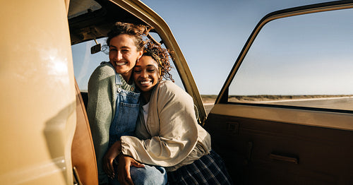 Two friends embrace inside a vintage van during a sunny road trip