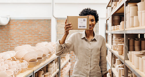 Happy female ceramist holding a biodegradable box in her shop