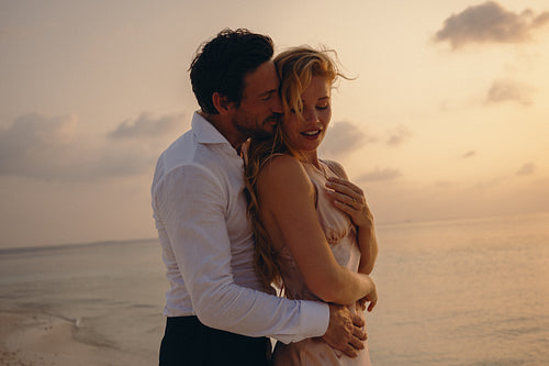 Young couple embracing during sunset on the beach, showcasing love and luxury