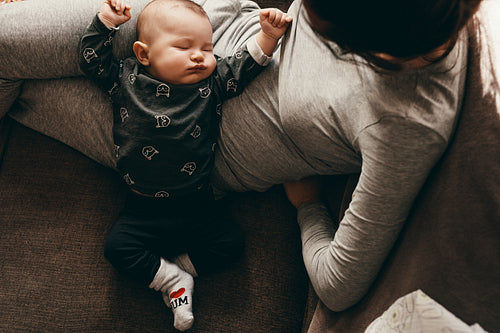 Mother sitting on couch with her baby sleeping on her